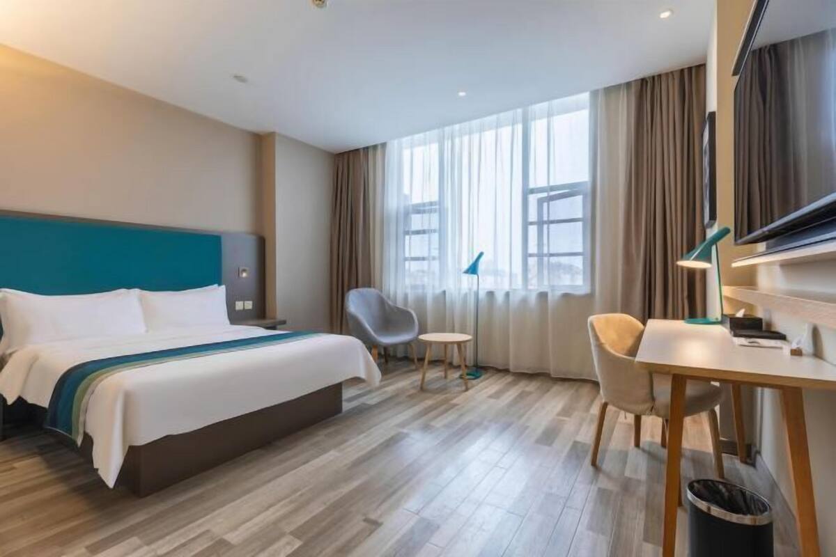 A hotel room with a bed, a desk, a chair, a TV, and a window with curtains.