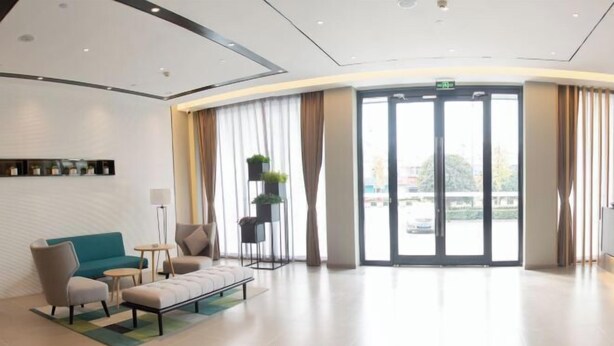 A modern hotel lobby with a curved reception desk, seating area with sofas and chairs, a small table, and a large glass door leading outside. - Homeinn Selected Hotel (Chuzhou Mingguang Mingzhu Avenue Zhengyuan Plaza) (Mingguang)