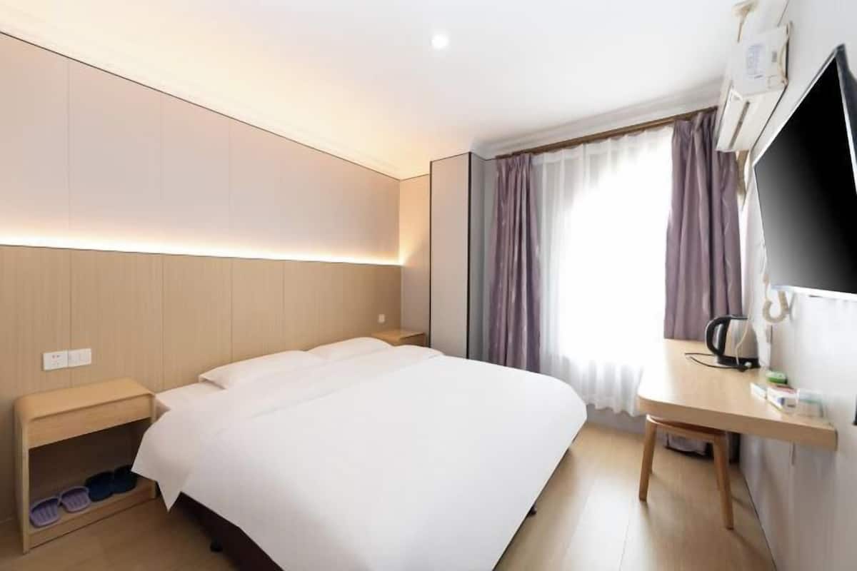 A hotel room with a bed, a desk, a chair, a TV, and a window with curtains.