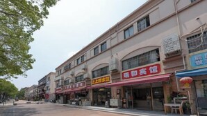 A street view with multiple storefronts, including a restaurant with a red awning and a sign in a foreign language. - Ruihe Hostel (Shanghai)