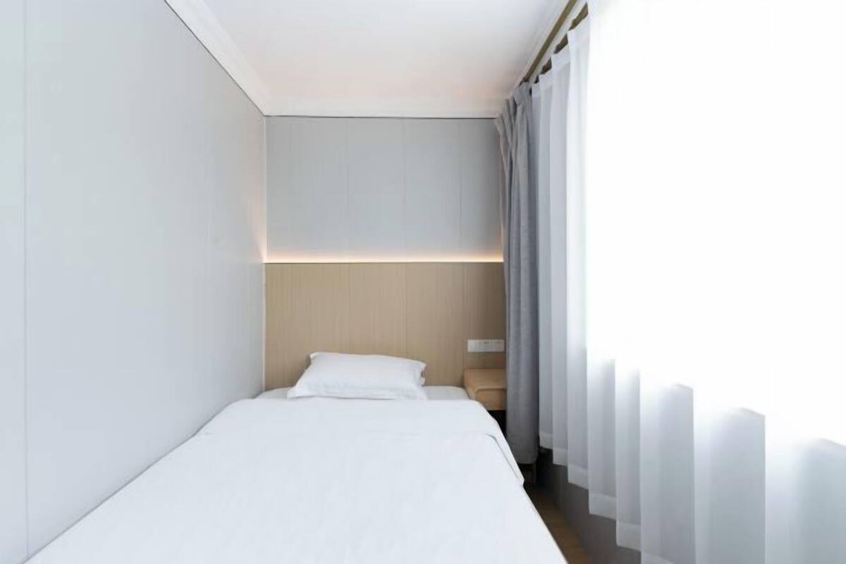 A modern hotel room with a bed, a bedside table, and a window with curtains.