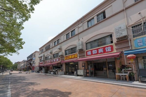 A street with multiple storefronts, including a restaurant with a red awning and a sign that reads '上饶老酒'. - Ruihe Hostel (Shanghai)