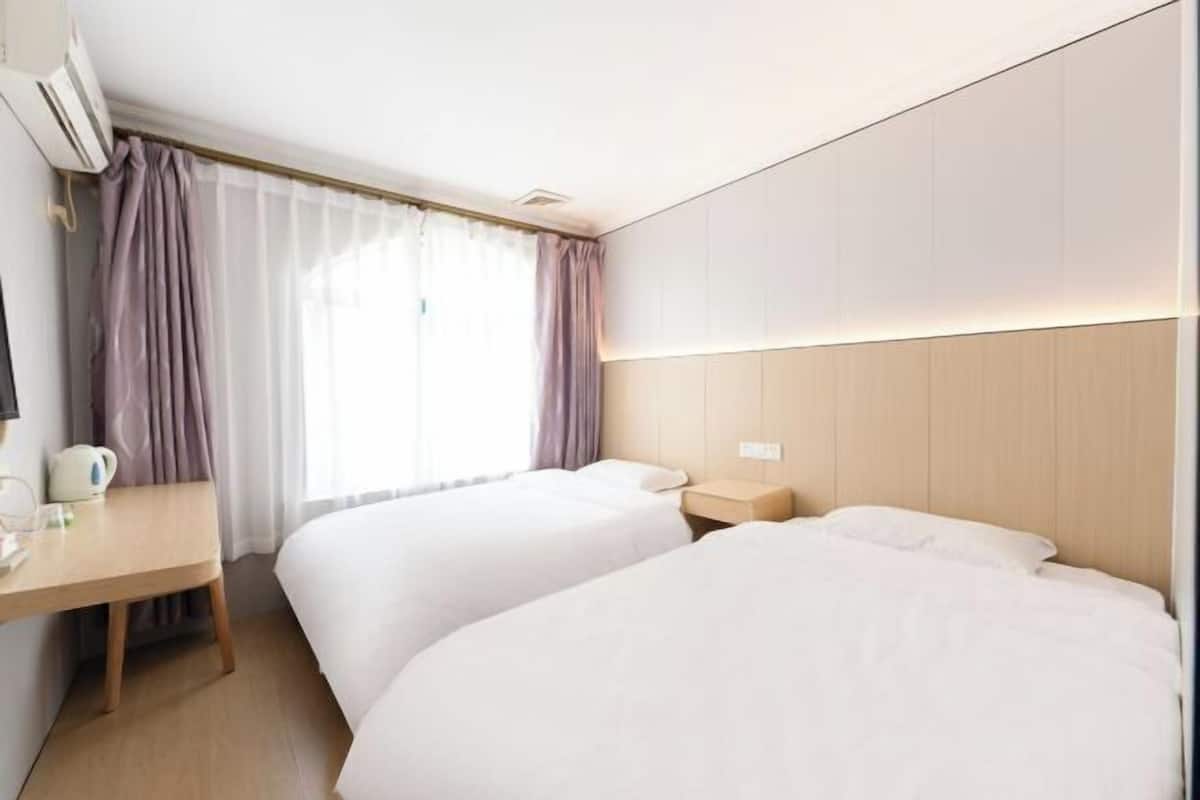 A hotel room with two beds, a desk, and a window with curtains.