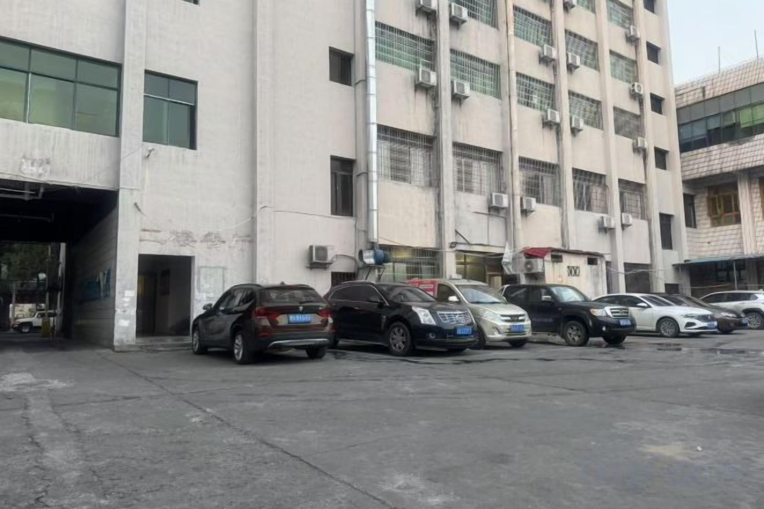 Un estacionamiento con varios coches aparcados frente a un edificio de varios pisos y unidades de aire acondicionado.