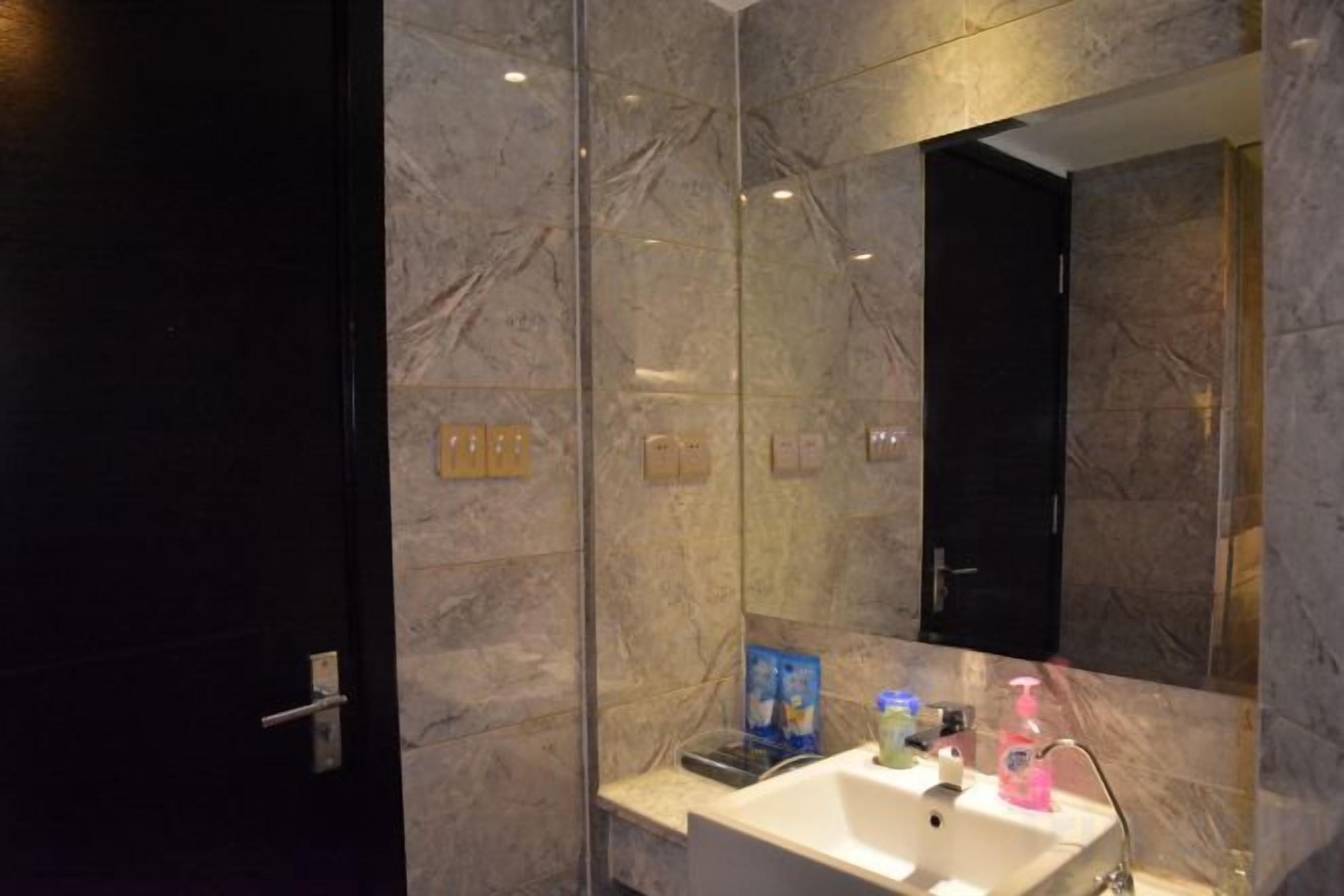 A modern bathroom with a marble wall, a glass shower enclosure, and a white sink with a mirror.