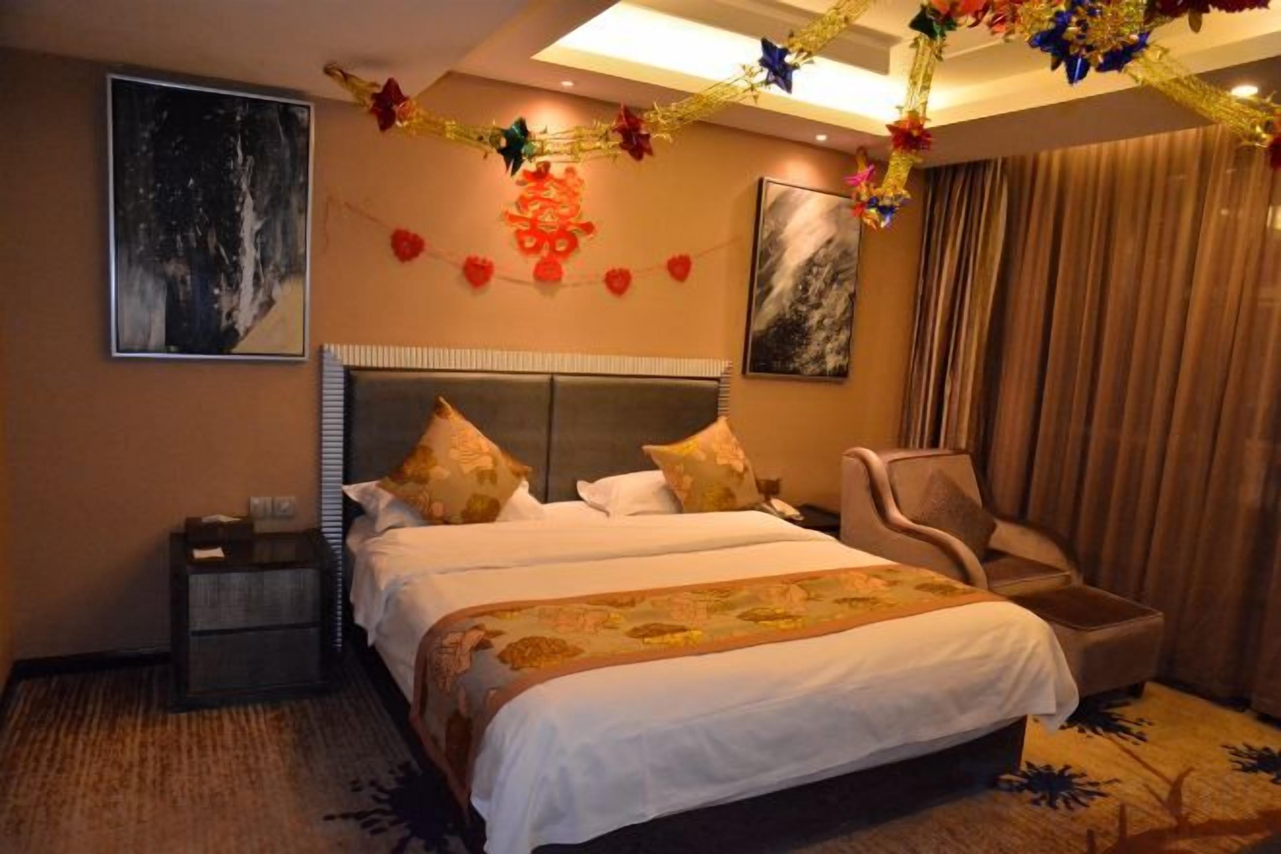 A hotel room with a large bed, a chair, a nightstand, and artwork on the walls.