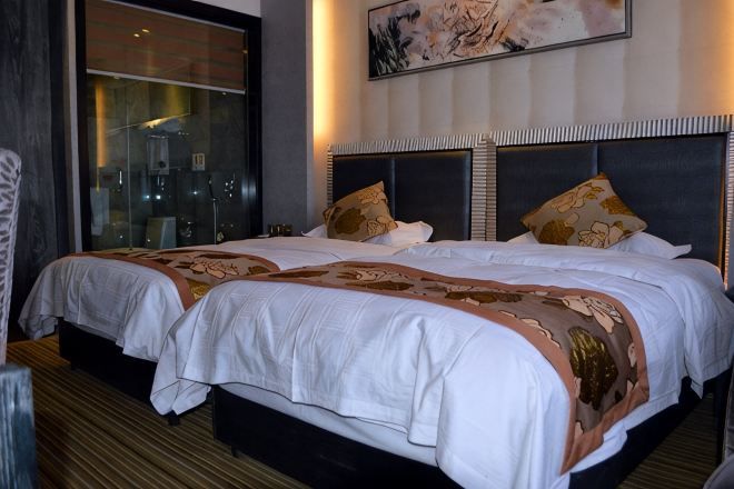 A double bed with a headboard, a window with a view, and a painting on the wall.