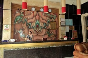 A reception desk with a decorative wall mural, a clock, and a sign indicating a 24-hour service area. - Sijiwenhua Hotel (Feicheng)