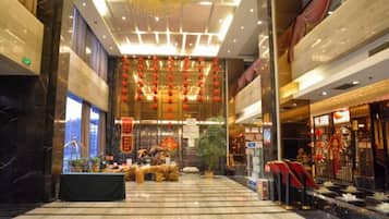 Un hall amplio con suelo de mármol, una zona decorativa central con plantas y un techo con adornos colgantes.