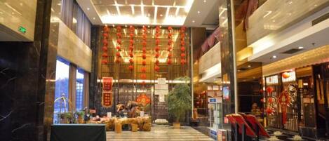 A spacious lobby with a marble floor, a central decorative area with plants, and a ceiling with hanging ornaments.