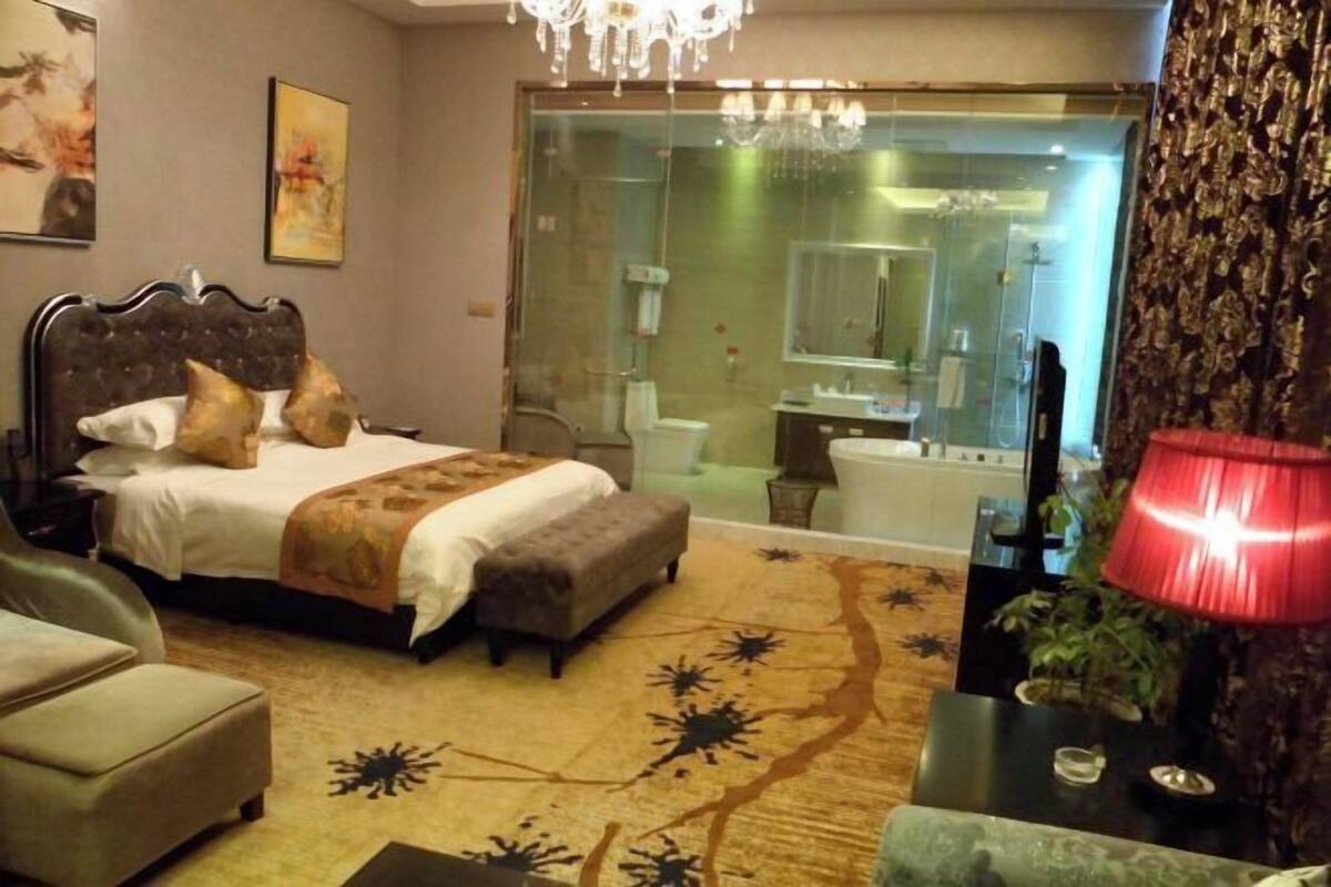 A bedroom with a bed, a chair, a bedside table, and a large window.