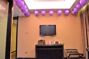 A room with a television mounted on the wall, a reception desk, and a window with curtains.