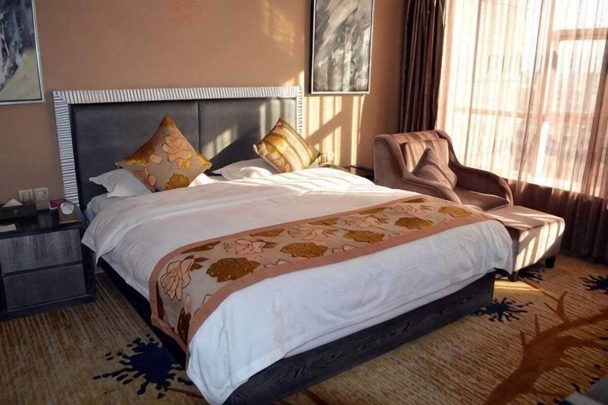 A hotel room with a large bed, a nightstand, a chair, and a window with curtains.