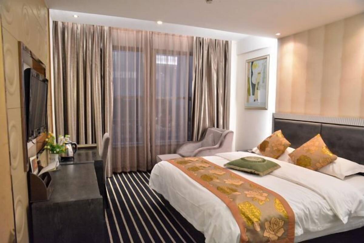 A hotel room with a bed, a desk, a chair, and a large window with curtains.