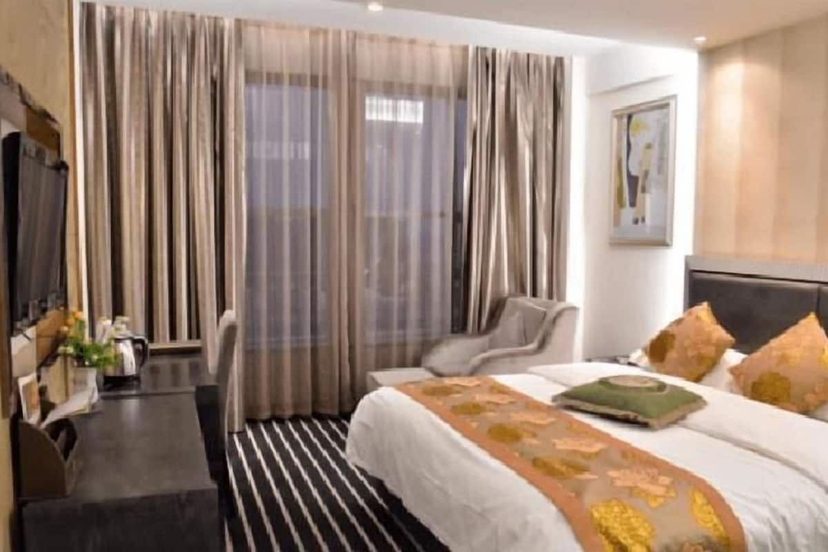 A hotel room with a bed, a chair, a desk, and a large window with curtains.