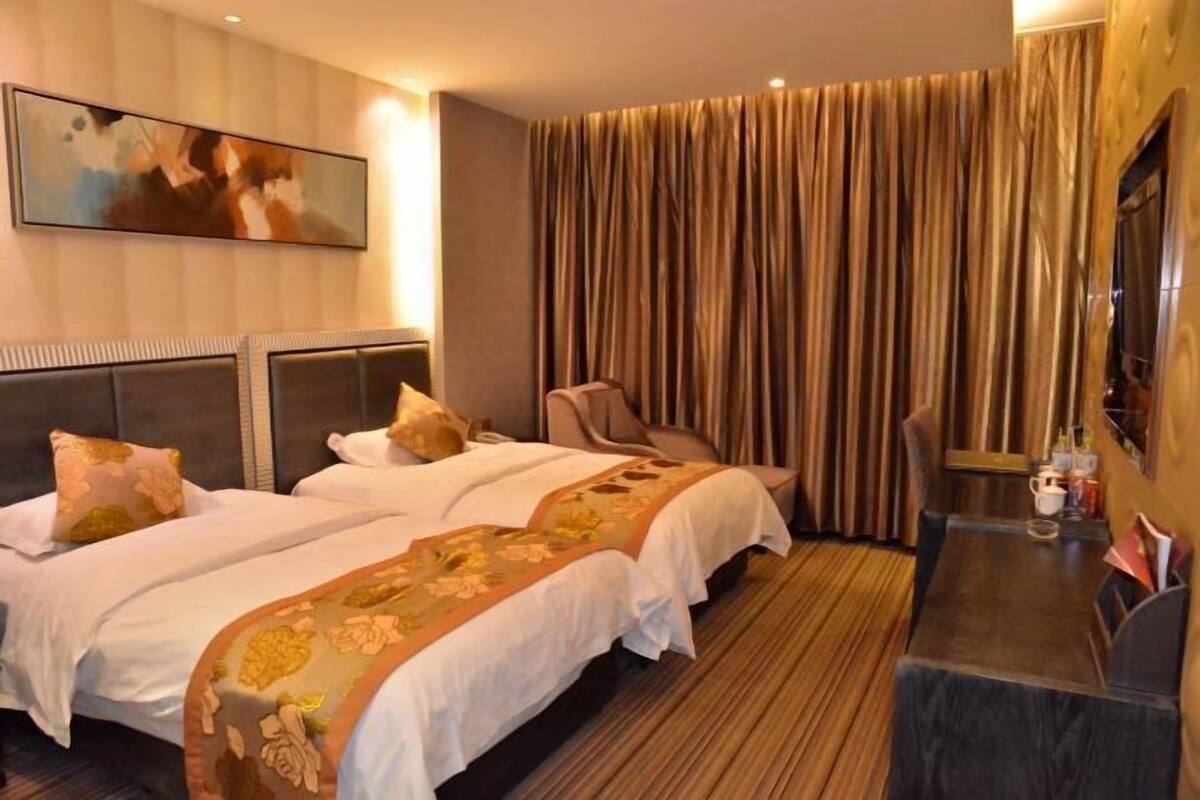 A hotel room with two beds, a large window with curtains, a flat-screen TV, and a small table with a chair.
