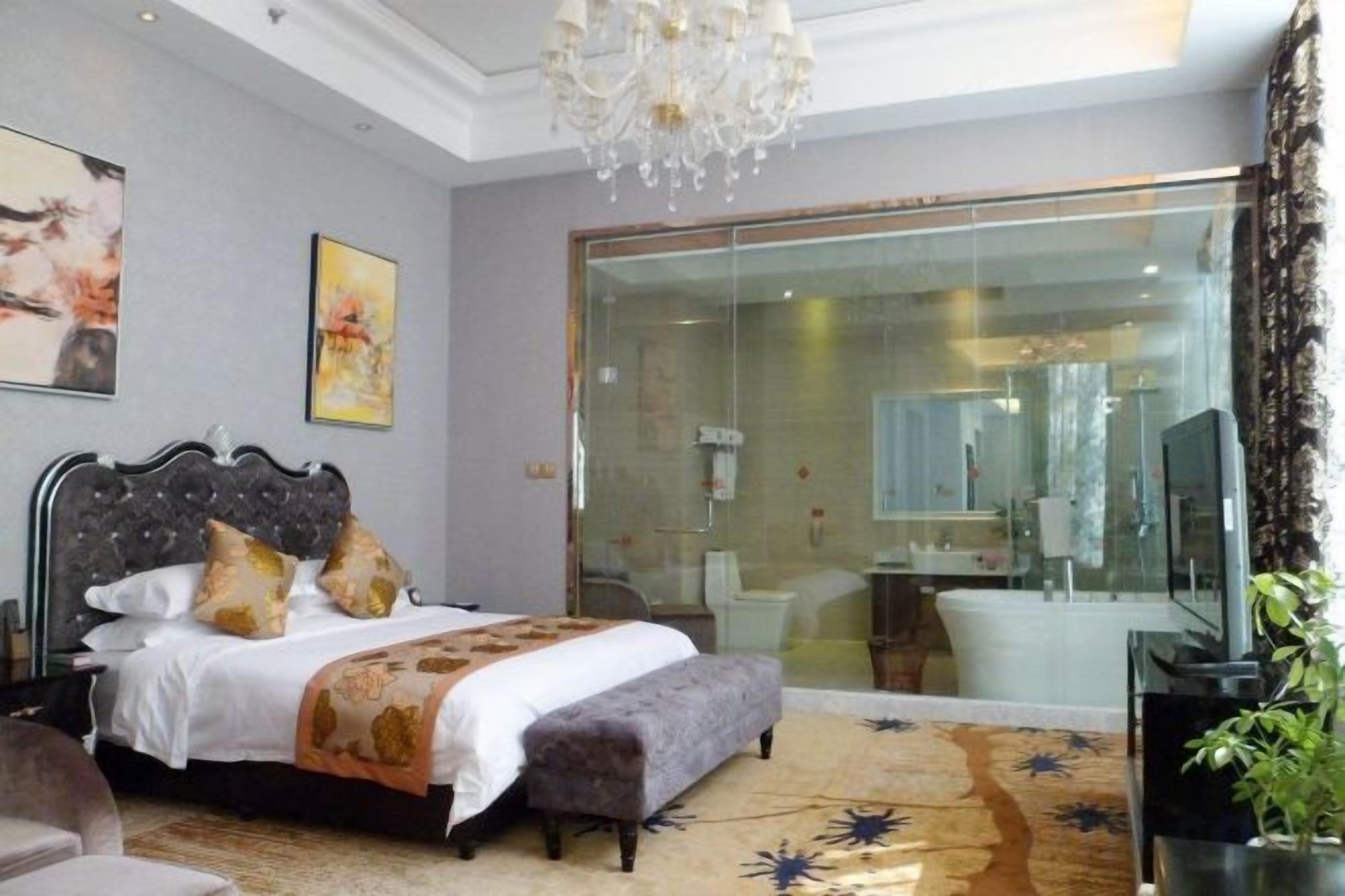 Un dormitorio con cama, un banco, una araña y una puerta corrediza de vidrio que da a un baño.