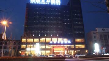 Un hotel de varios pisos con un letrero llamativo en la parte superior, una entrada bien iluminada y un estacionamiento al frente.