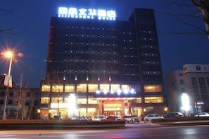 A multi-story hotel with a prominent sign at the top, a well-lit entrance, and a parking area in front. - Sijiwenhua Hotel (Feicheng)