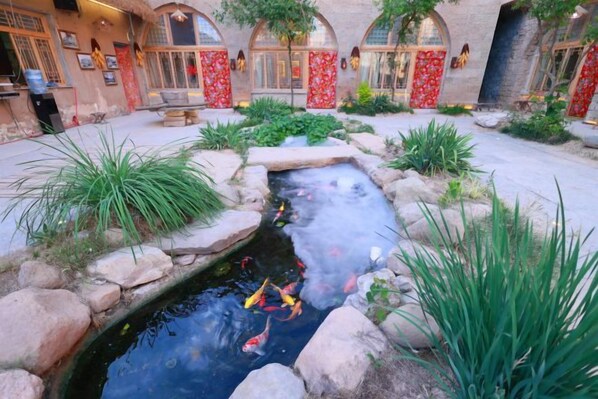 A courtyard with a small pond, stone pathway, and red decorative elements.