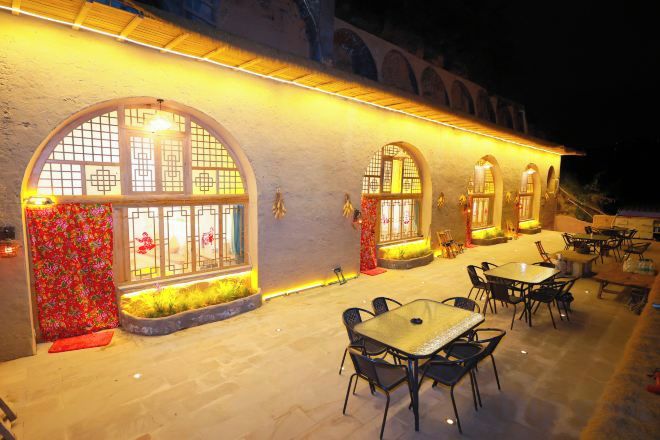 An outdoor dining area with tables and chairs, large arched windows, and a building facade.
