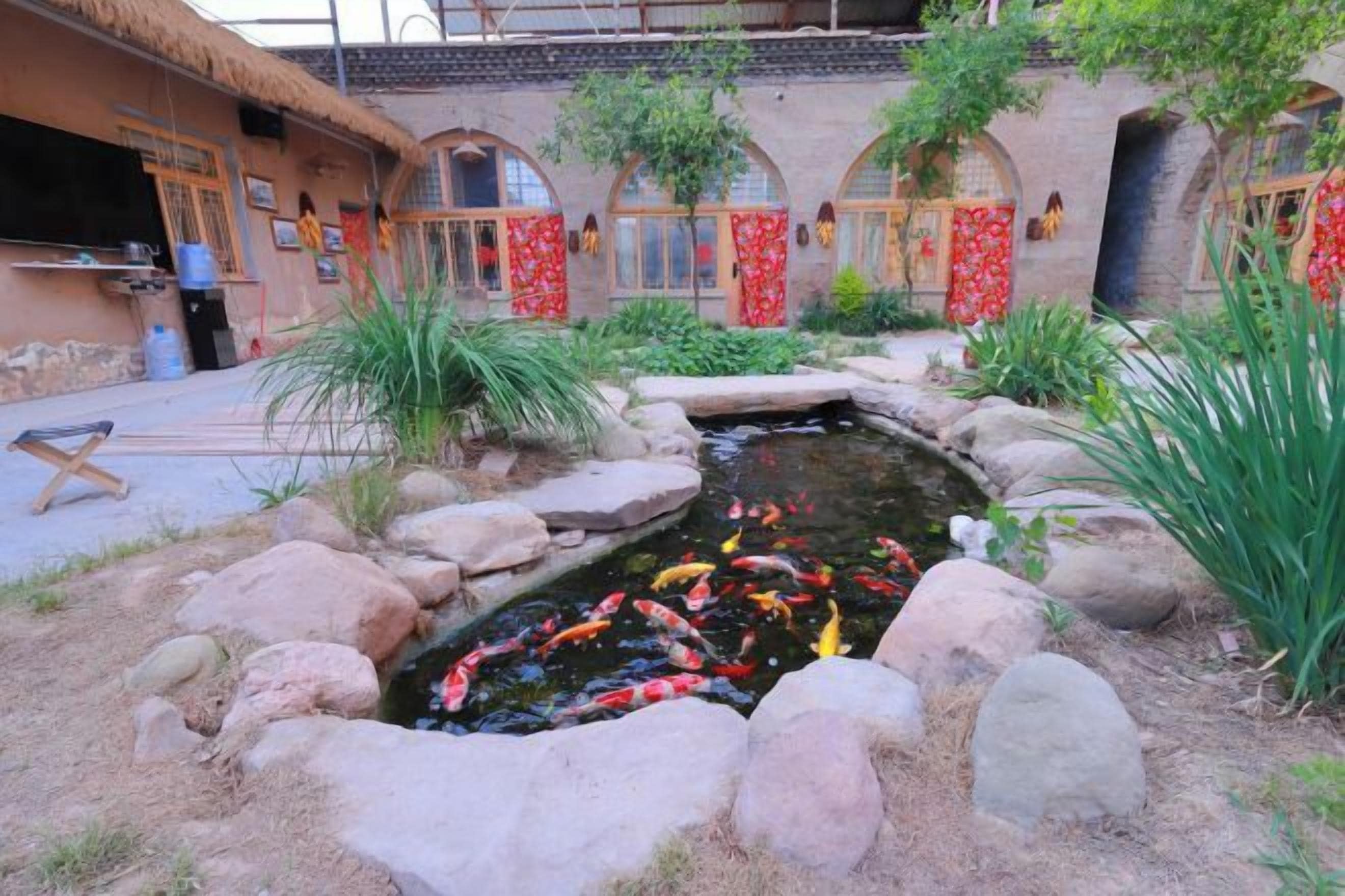 A koi pond with rocks and plants, a thatched-roof building, and red decorations.