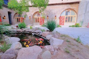 A courtyard with a pond, rocks, and a building with arched windows and red decorations.