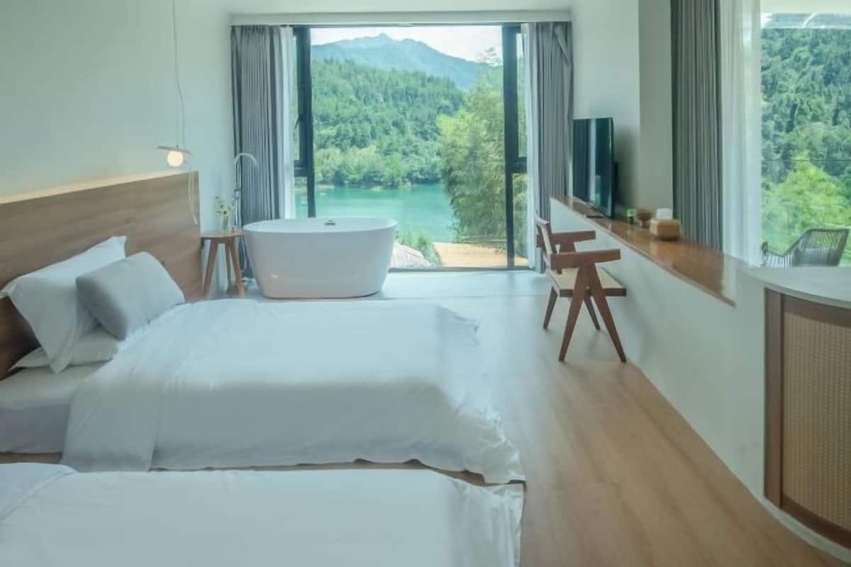 A bedroom with a large bed, a bathtub, a desk, and a view of a lake and mountains.