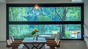 A dining area with a table and chairs, a vase with a sunflower, and a large window with a view of trees and a stone wall. - Hi Ta B&B (Chun'an)