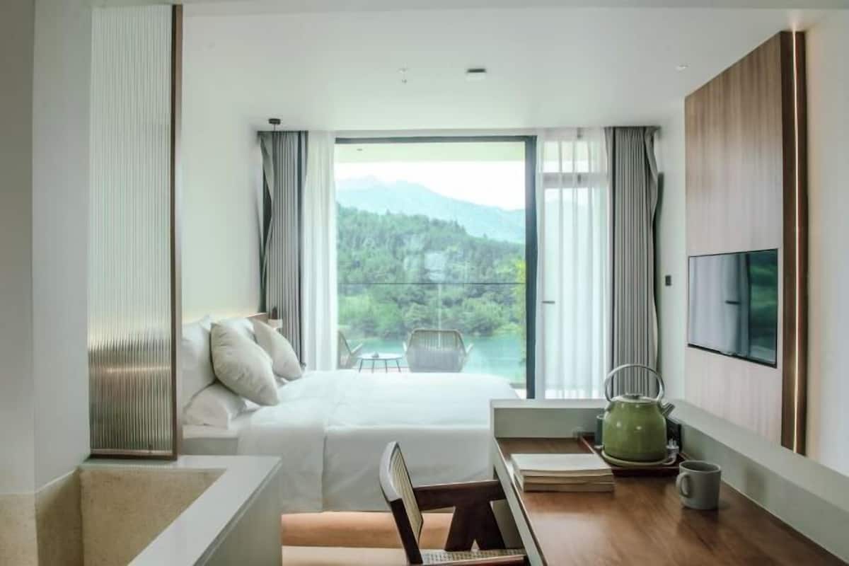 A modern hotel room with a large bed, a desk with a kettle, and a TV on the wall.