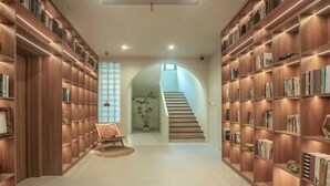 A library with bookshelves on both sides, a staircase in the center, and a chair in the foreground. - Hi Ta B&B (Chun'an)
