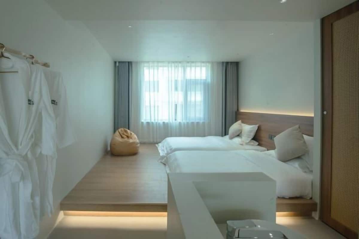 A hotel room with two beds, a seating area, a wardrobe, and a window with curtains.