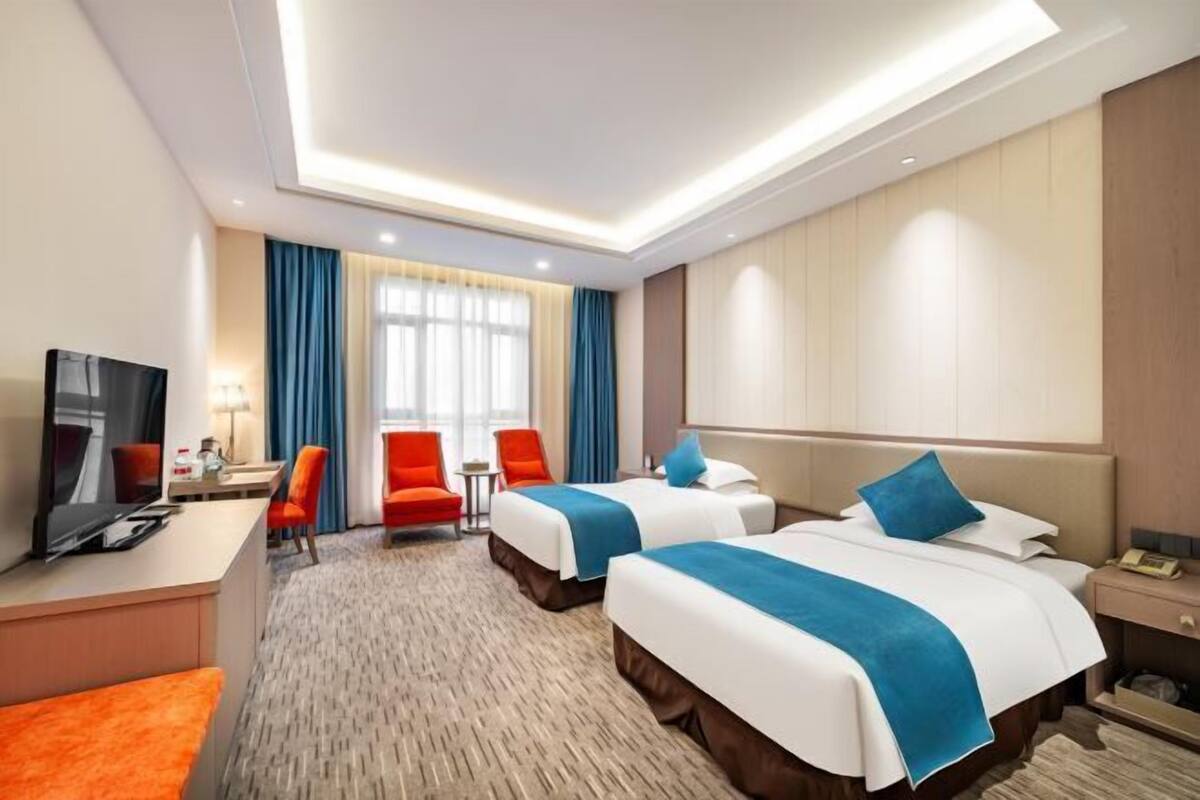 A hotel room with two beds, a desk, a TV, and a seating area.