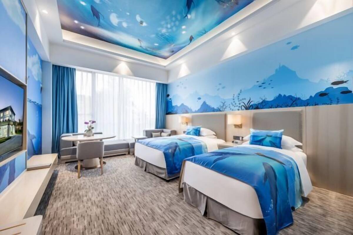A hotel room with two beds, a desk, and a large window.