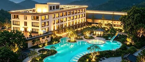 A hotel with a large swimming pool, surrounded by lush greenery and mountains in the background.