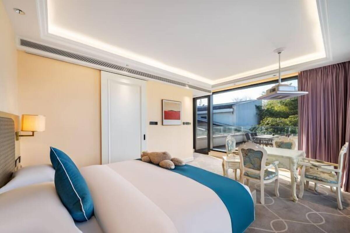 A hotel room with a bed, a desk, and a balcony with outdoor seating.