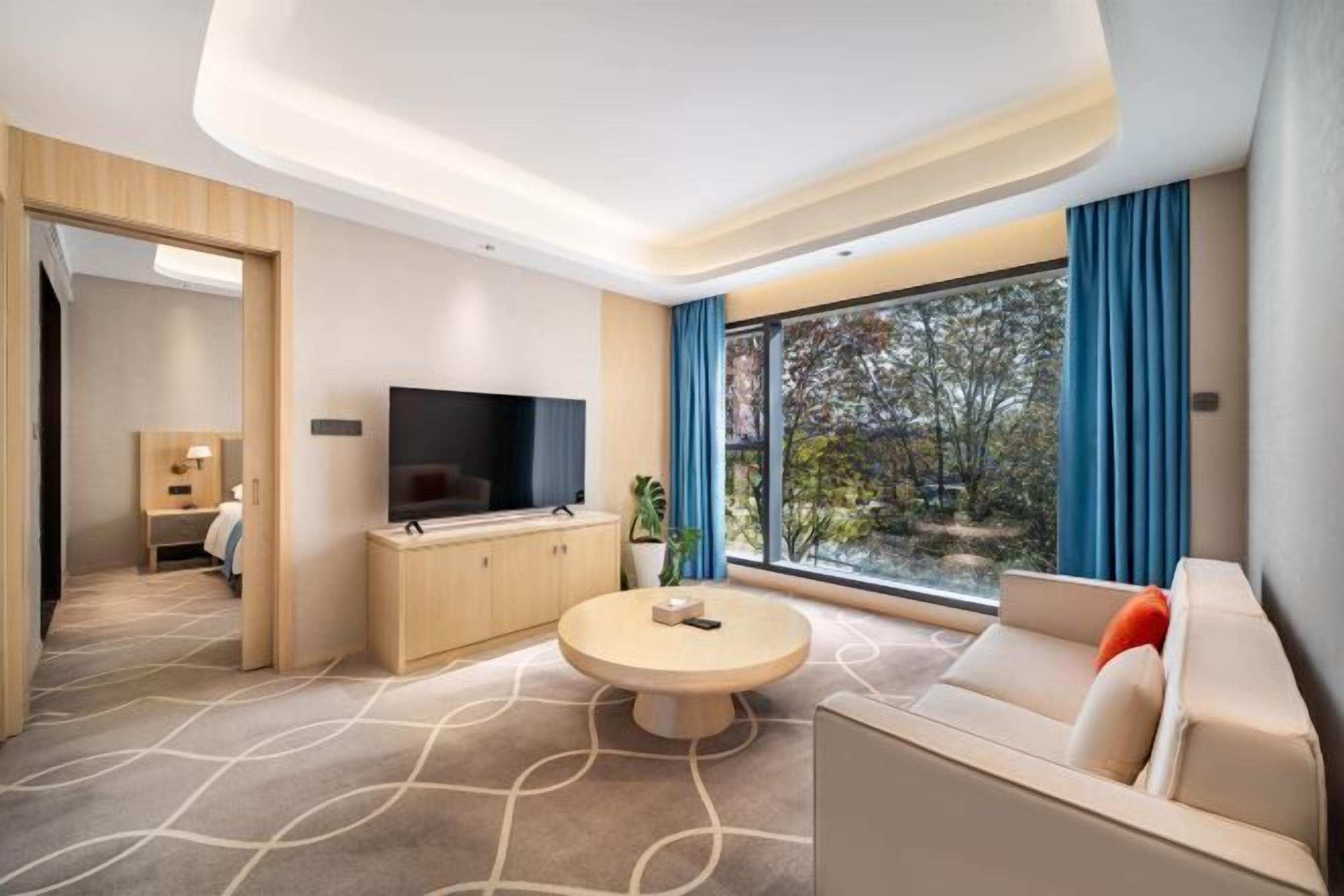 A modern living room with a round coffee table, a sofa, a TV, and a large window with curtains.
