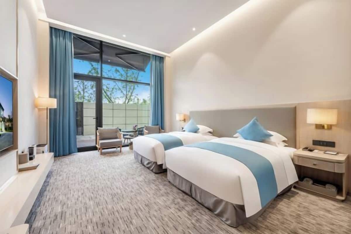 A hotel room with two beds, a desk, a chair, and a large window.