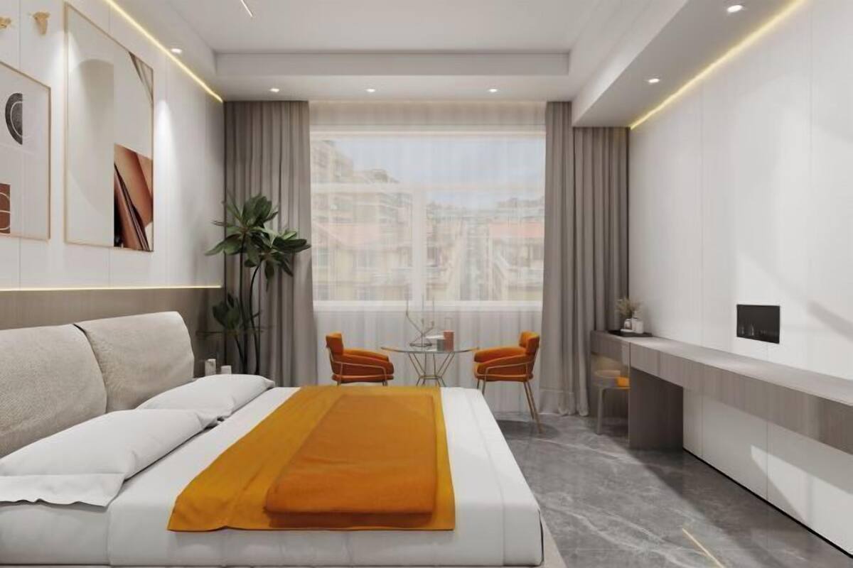 Habitación de hotel moderna con cama, una mesita, dos sillas, una planta y vistas a edificios.