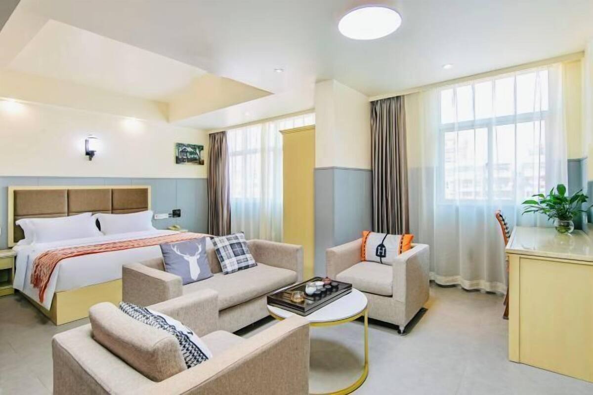 Una habitación de hotel con una cama, dos sofás, una mesa de centro, un escritorio y un ventanal con cortinas.