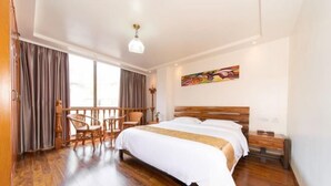 Camera d'albergo con un letto grande, pavimento in legno, un balcone con sedie e un quadro appeso al muro.
