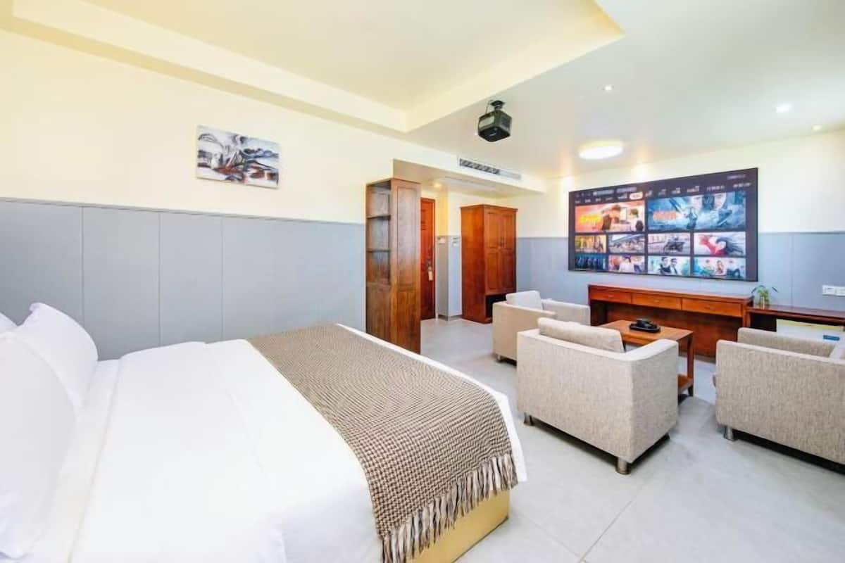 Habitación de hotel con cama, dos sofás, escritorio y una pantalla de televisión grande.