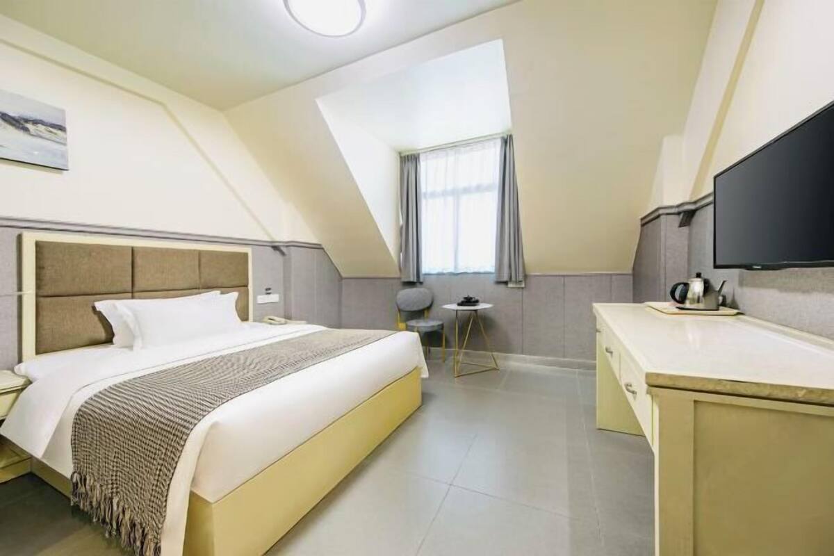 Habitación de hotel moderna con cama, escritorio, silla, televisor y ventana con cortinas.