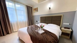 Una camera d'albergo con un letto grande, un comodino, una lampada a parete e una finestra con tende.