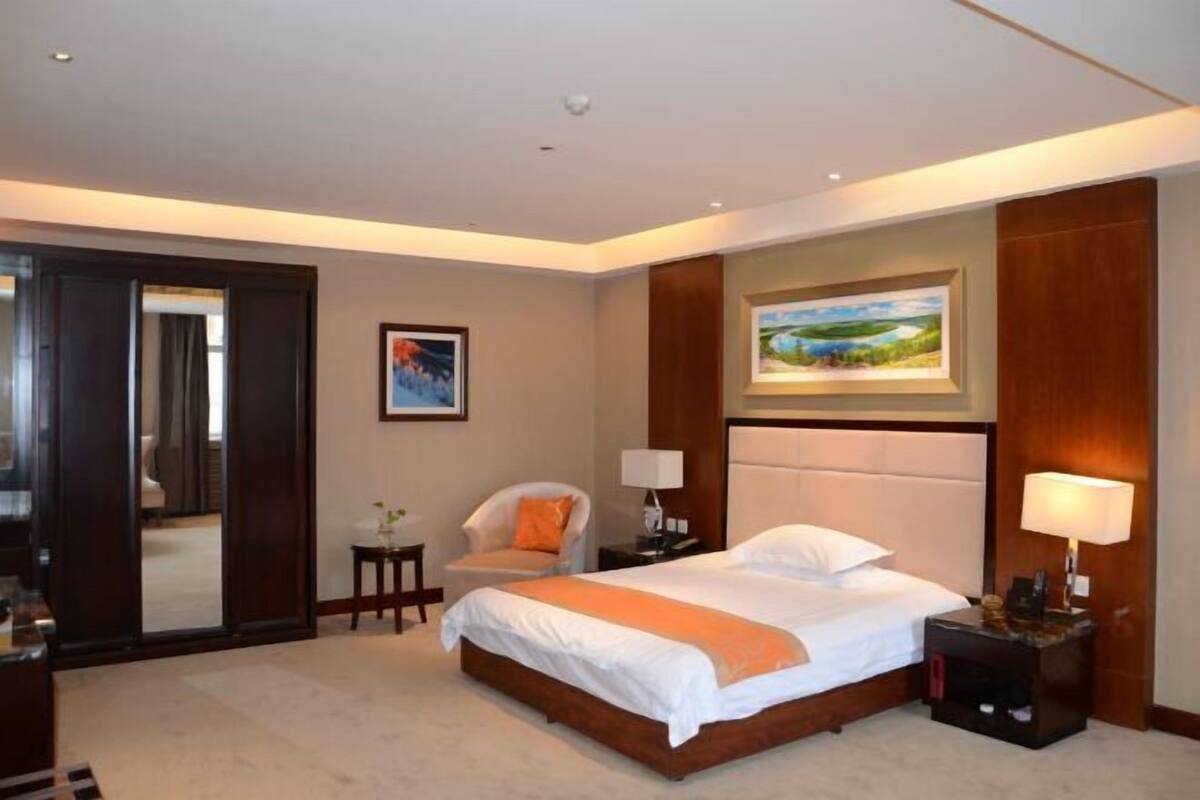 A hotel room with a large bed, a chair, a nightstand, a lamp, and a painting on the wall.
