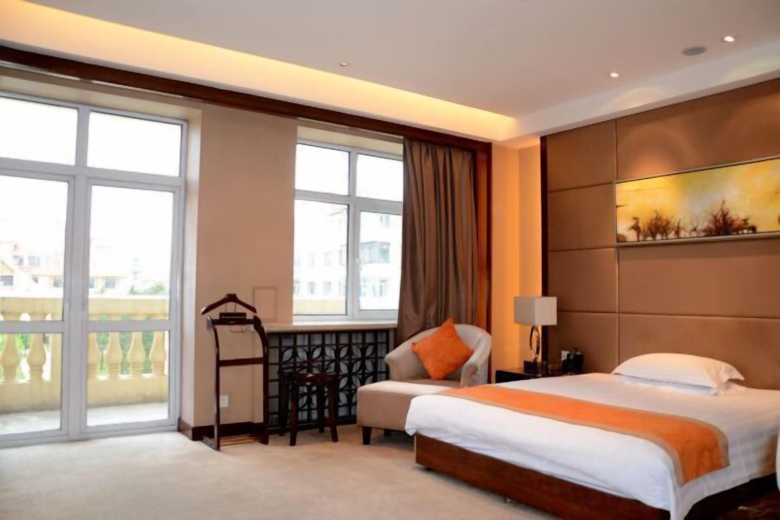 A hotel room with a bed, a desk, a chair, a window with a view, and a painting on the wall.