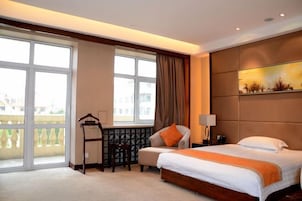A hotel room with a bed, a desk, a chair, a window with a view, and a painting on the wall.