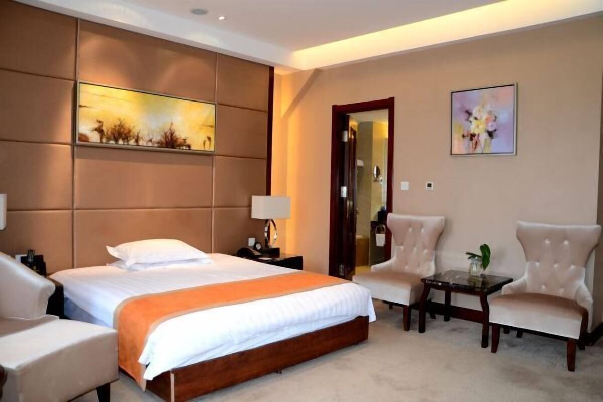 A hotel room with a large bed, two armchairs, a small table, a nightstand, and artwork on the walls.