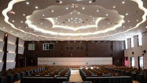 A large conference room with rows of tables and chairs, a modern ceiling design, and large windows on one side. - Mohe International Conference Center (Mohe)
