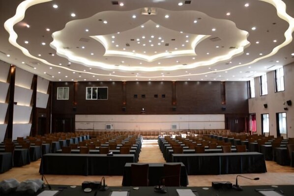 A large conference room with rows of tables and chairs, a modern ceiling design, and large windows on one side. - Mohe International Conference Center (Mohe)